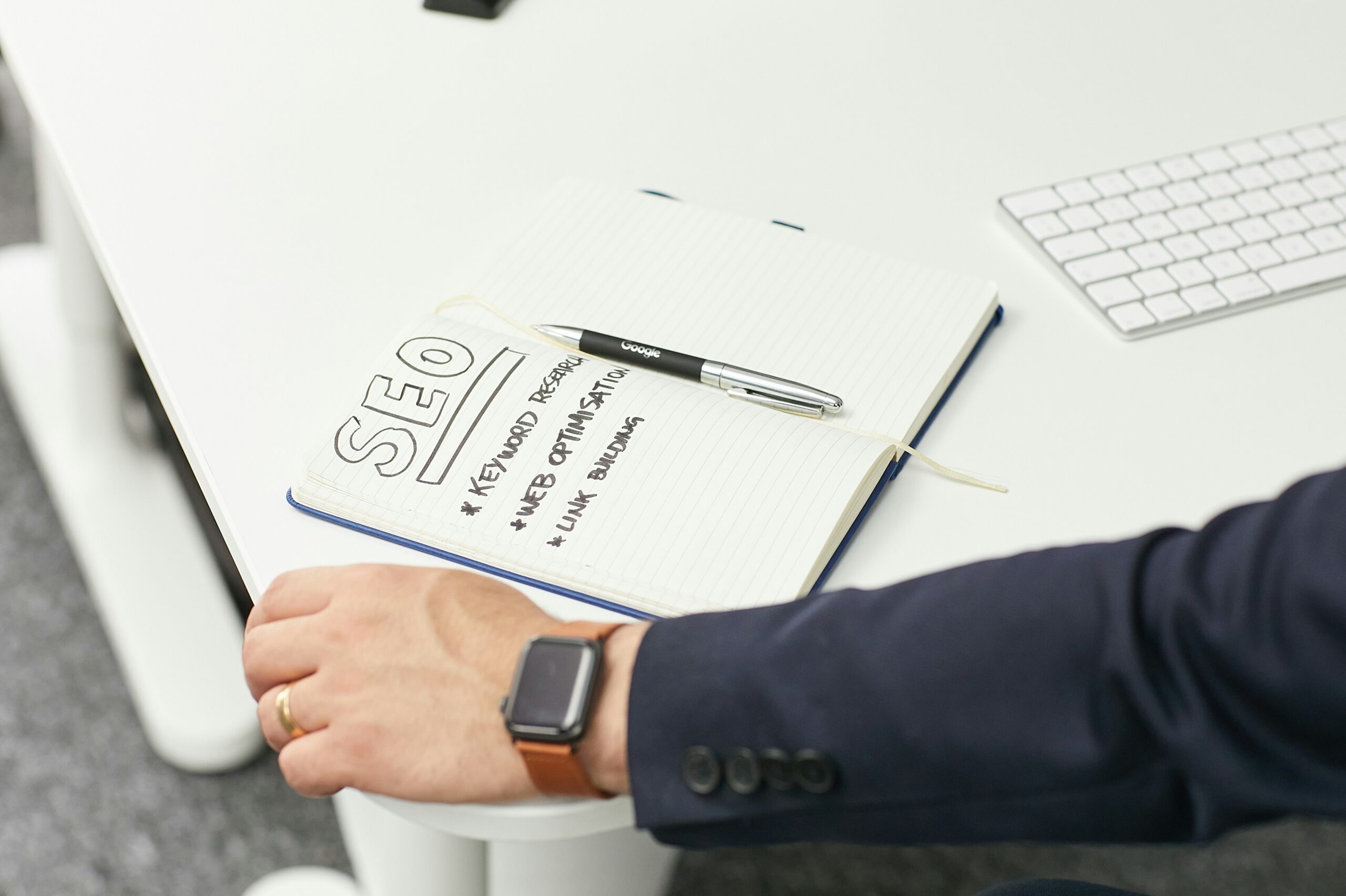 A marketer planning their SEO strategy in a notebook, with the title SEO underlined and three bullet points: keyword research, web optimisation, link building.